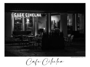 Café Cihelna - Černobílá fotografie kavárny Cafe Cihelna v Praze, osvětlený interiér a prázdné venkovní posezení v nočním prostředí, autor Martin Lukač