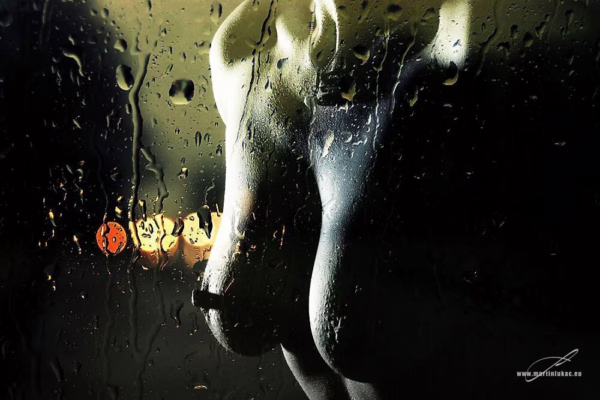 Silueta ženy za mokrým sklem s kapkami deště, za kterým se rozmazaně rýsují světla v pozadí, autor Martin Lukač, www.martinlukac.eu, barevná