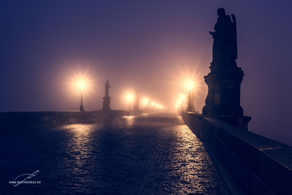 Noční Karlův most zalitý mlhou a světlem luceren, s dramatickými siluetami soch, autor Martin Lukač