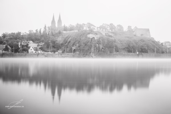 Mlžný pohled na historickou pevnost Vyšehrad s dvojvěžím baziliky sv. Petra a Pavla, odraz ve Vltavě, autor Martin Lukač, černobílá
