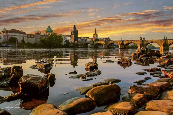 Karlův most za ranního světla od břehu Vltavy mezi kameny, autor Martin Lukač, pražský fotograf, www.martinlukac.eu