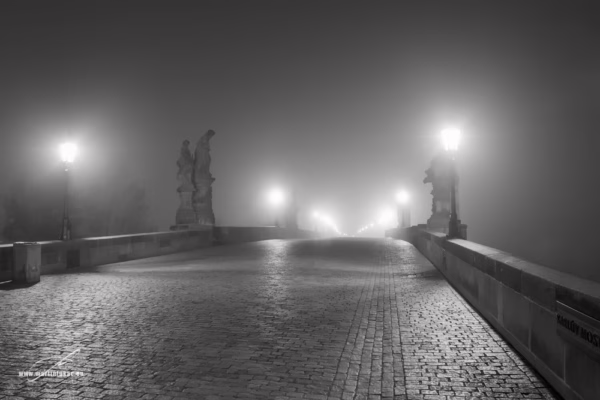 Noční Karlův most zahalený mlhou, osvětlený lucernami, bez lidí, autor Martin Lukač, černobílá