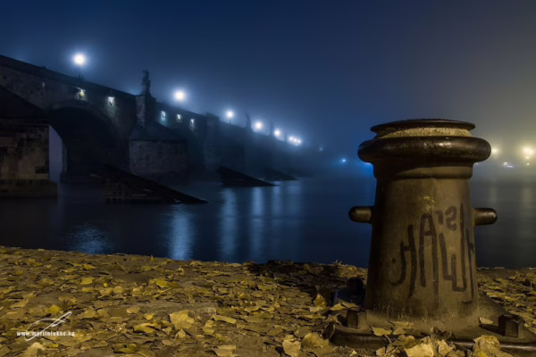 Karlův most v mlžné modré noci, v popředí nábřeží s vázacím sloupkem, fotografie s podzimní atmosférou, autor Martin Lukač