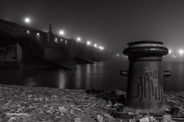 Karlův most v mlžné modré noci, v popředí nábřeží s vázacím sloupkem, fotografie s podzimní atmosférou, autor Martin Lukač, černobílá