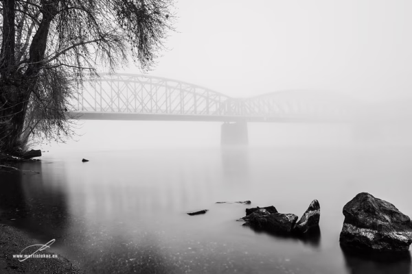 Černobílá fotografie železničního mostu přes Vltavu v ranní mlze, chladná atmosféra a klidná voda, autor Martin Lukač, černobílá
