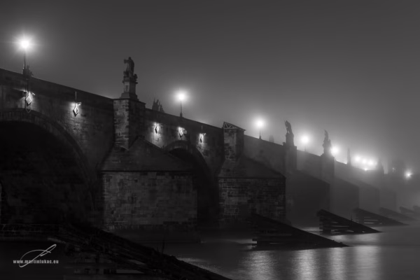 Karlův most v noci zahalený mlhou a osvětlený lucernami, poetická noční fotografie, autor Martin Lukač, černobílá