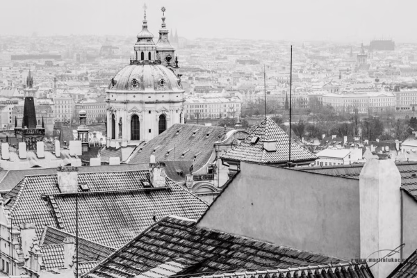 Černobíle laděná fotografie zasněžené Malé Strany s věží sv. Mikuláše, autor Martin Lukač