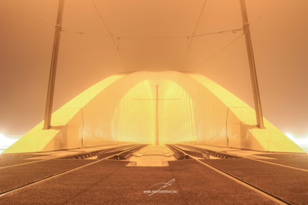 Černobílá fotografie Trojského mostu v mlze s tramvajovými kolejemi a osvětlenou konstrukcí, autor Martin Lukač