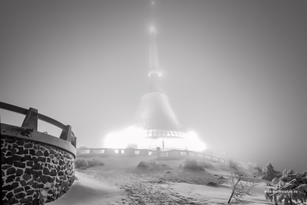 Ufo na Ještědu – Zasněžený vrchol Ještědu s nasvícenou televizní věží v mlze, autor Martin Lukač, černobílý