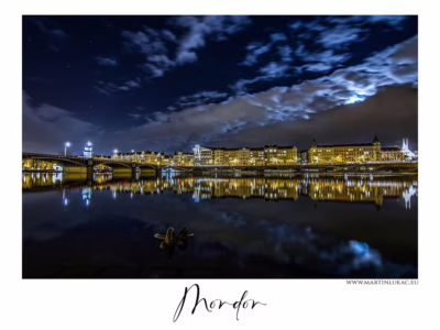 Noční Praha s dramatickou oblohou... Noční panorama Prahy s mostem a osvětlenými budovami odrážejícími se ve Vltavě, autor Martin Lukač