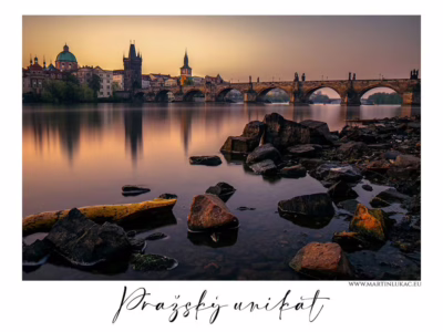 Pražský unikát – Dominanty Starého Města... Karlův most v zlatém světle ranního úsvitu přes řeku Vltavu, v popředí klidná hladina a kameny, autor Martin Lukač